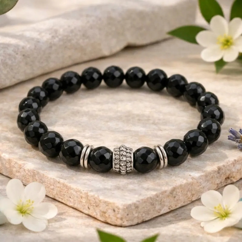 Black beaded bracelet with a silver clasp on a stone surface with flowers