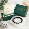 Black beaded bracelet on a white stand with 'Calminds' packaging and guide book in the background.