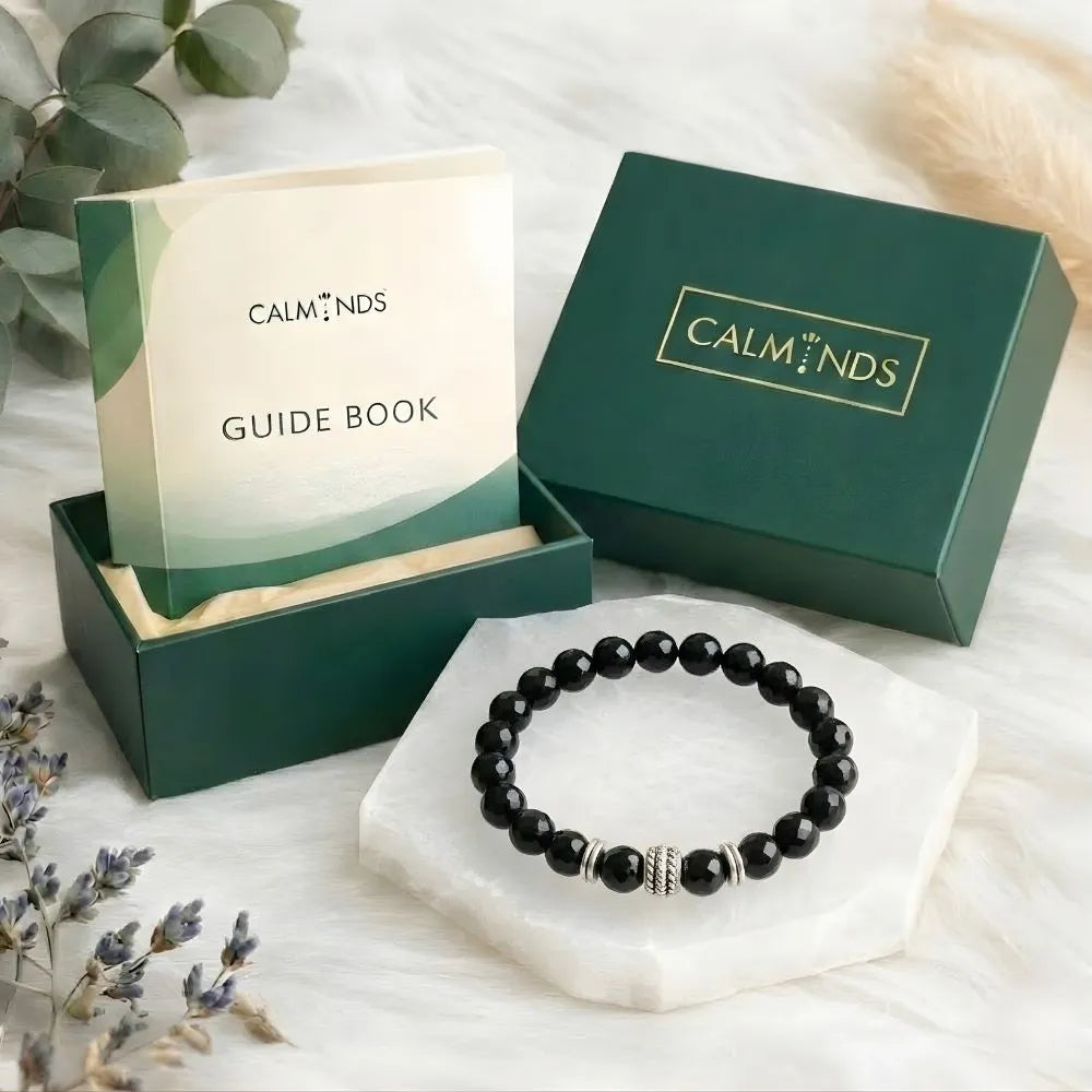 Black beaded bracelet on a white stand with 'Calminds' packaging and guide book in the background.