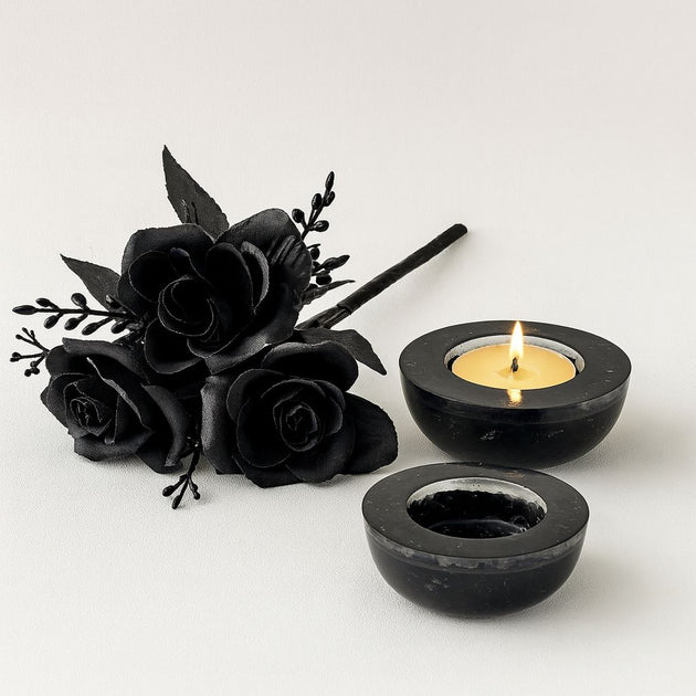 Black decorative roses and two black candle holders with a lit candle on a white background
