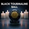 Black tourmaline ball with a gold symbol in front of lit candles on a dark background