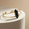 Gold bracelet with a black gemstone on a beige background