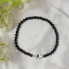Black beaded bracelet with a blue evil eye charm on a white fabric background