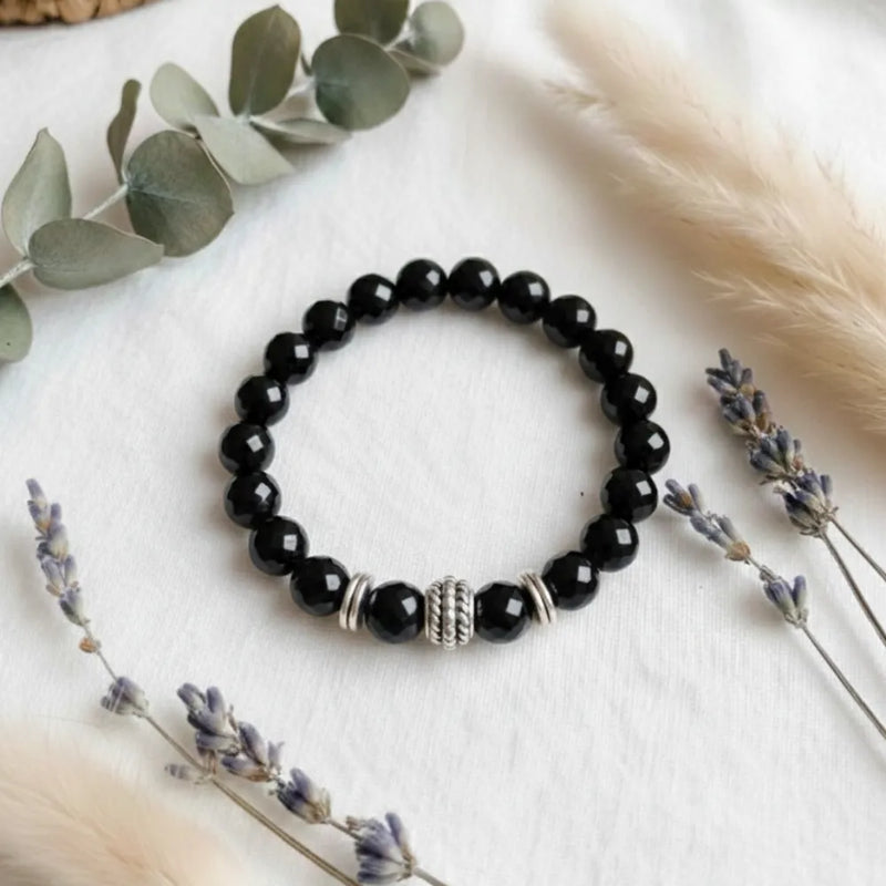 Black beaded bracelet with silver accents on a white surface with decorative elements.