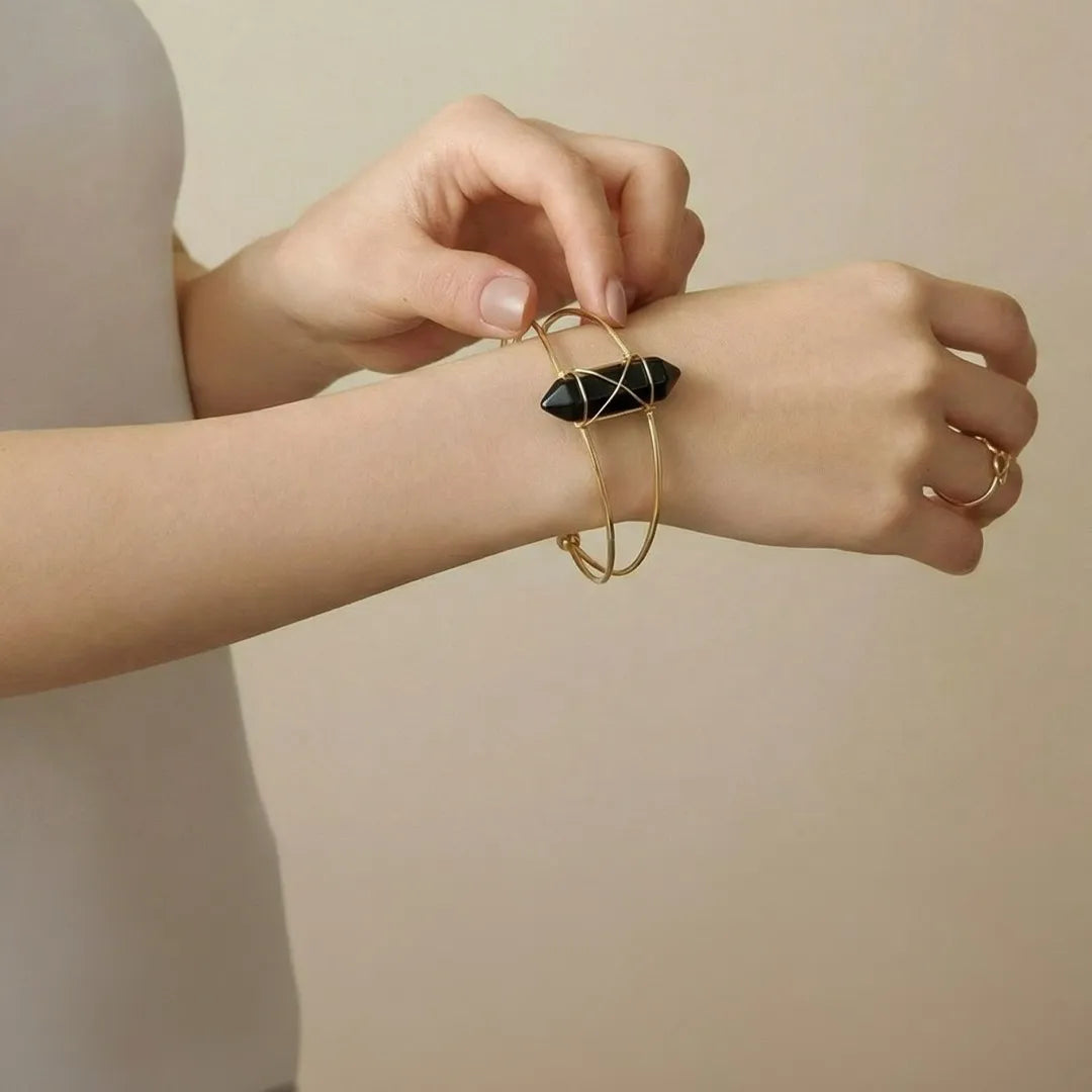 Person wearing a gold bracelet with black stones on a neutral background