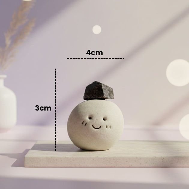 Ceramic ball with a small black rock on top, placed on a white surface with measurement labels.