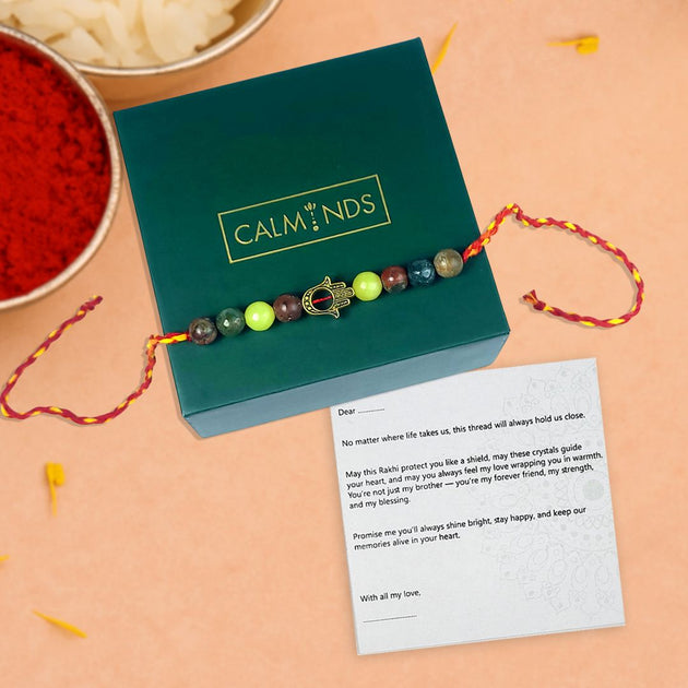 Crystal rakhi with a card on a green box labeled 'Calminds' on a beige background.