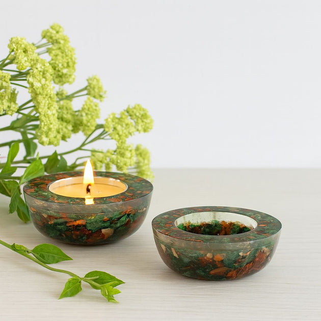 Two green marbled candle holders with a lit candle on a light surface with greenery.