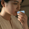 Woman holding a small white container to her mouth against a blurred background