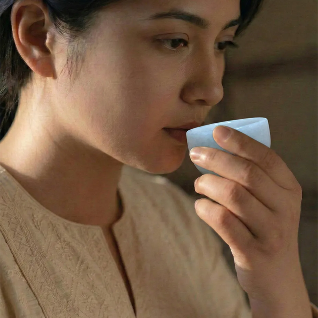 Woman holding a small white container to her mouth against a blurred background