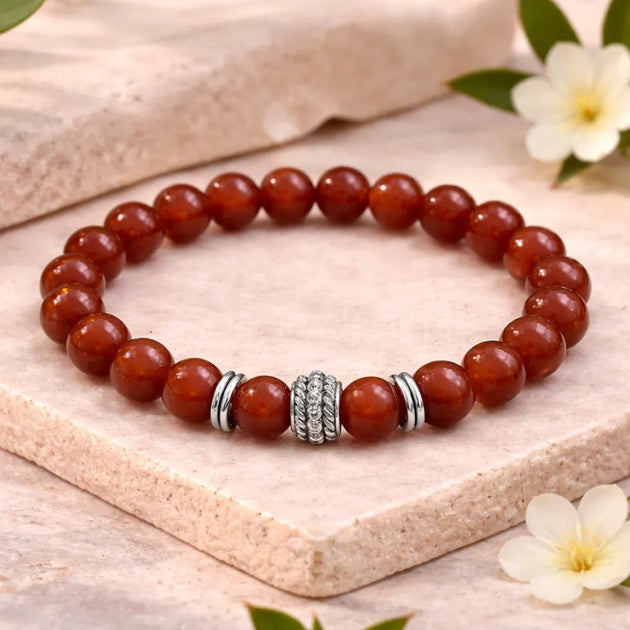 Red beaded bracelet with a silver clasp on a light wooden surface with flowers.