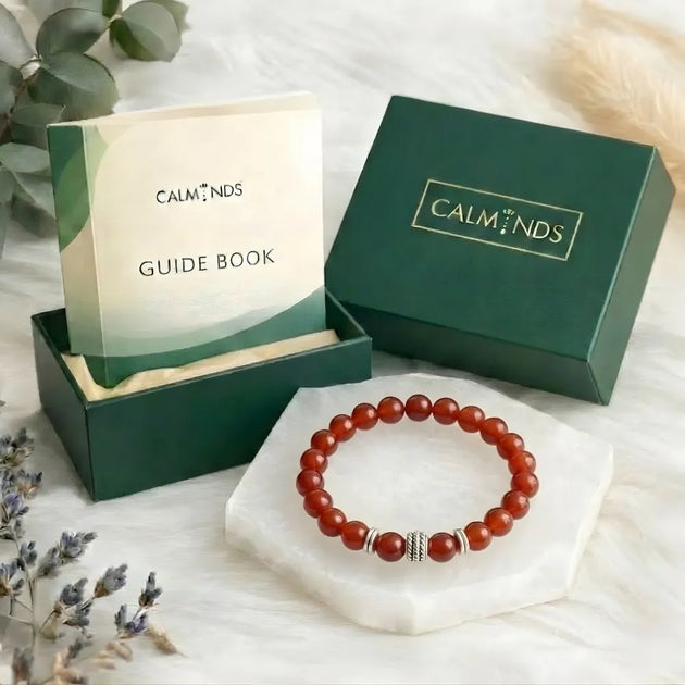 Red beaded bracelet on a white surface with 'Calminds' packaging and guide book.