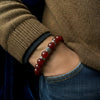 Close-up of a person wearing a red beaded bracelet with a brown sweater and blue jeans.