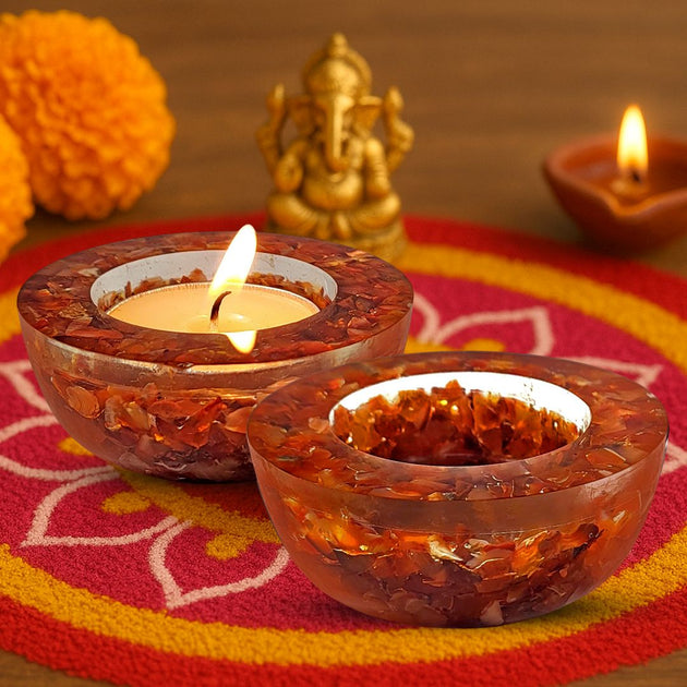 Decorative carnelian candle holders with candles on a colorful mat, featuring a small statue and marigold flowers.