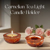 Carnelian tea light candle holder with a lit candle on a surface with flowers in the background.