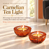 Two carnelian tea light holders with orange-red crystal chips and lit candles on a terrazzo floor