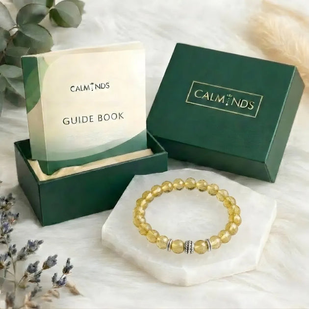 Yellow beaded bracelet with 'Calminds' packaging and guide book on a white surface.