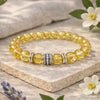 Yellow beaded bracelet with silver accents on a stone surface with flowers