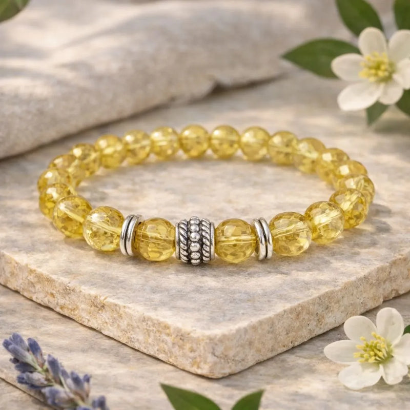 Yellow beaded bracelet with silver accents on a stone surface with flowers