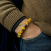 Yellow beaded bracelet on a wrist with a brown sweater and blue jeans.