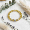 Yellow beaded bracelet on a white surface with eucalyptus and lavender.