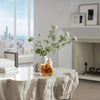Modern living room with a white marble coffee table, vase of flowers, and cityscape view.