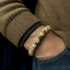 Close-up of a wrist wearing a beaded bracelet with a brown sweater and blue jeans.