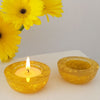 Two yellow candle holders with a lit candle and yellow flowers on a white surface