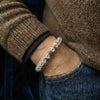 Close-up of a hand wearing a beaded bracelet with a brown textured sleeve and dark jeans.