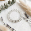 Clear beaded bracelet with silver accents on a white surface with lavender and eucalyptus leaves.