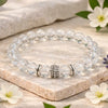 Clear beaded bracelet with silver charm on a stone surface with flowers
