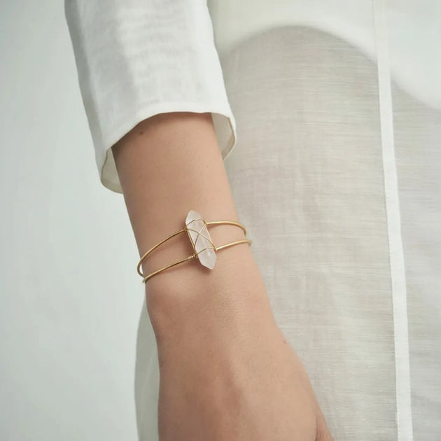 Gold bracelet with a stone on a wrist against a neutral background
