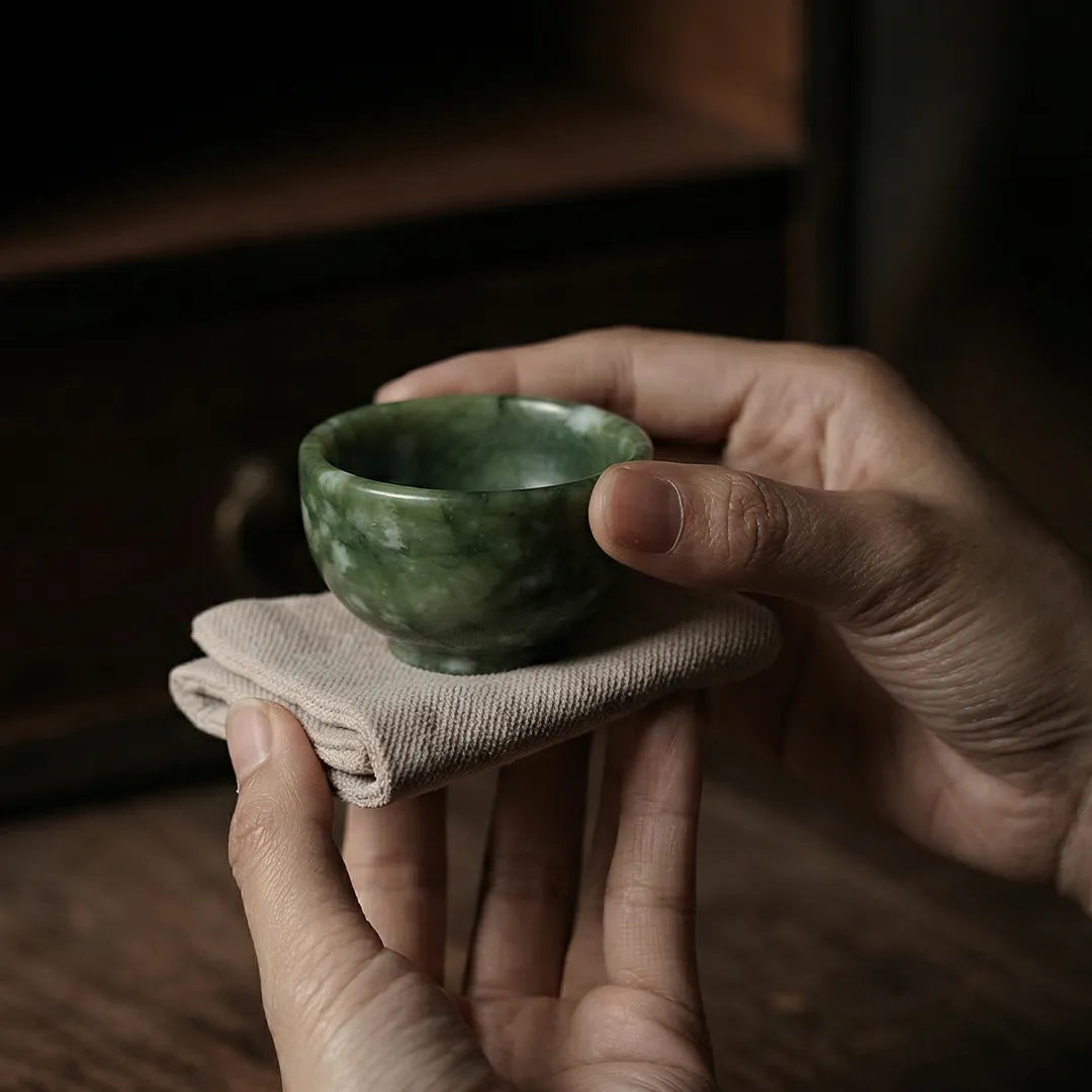 Person holding a small green stone bowl on a cloth with a dark background
