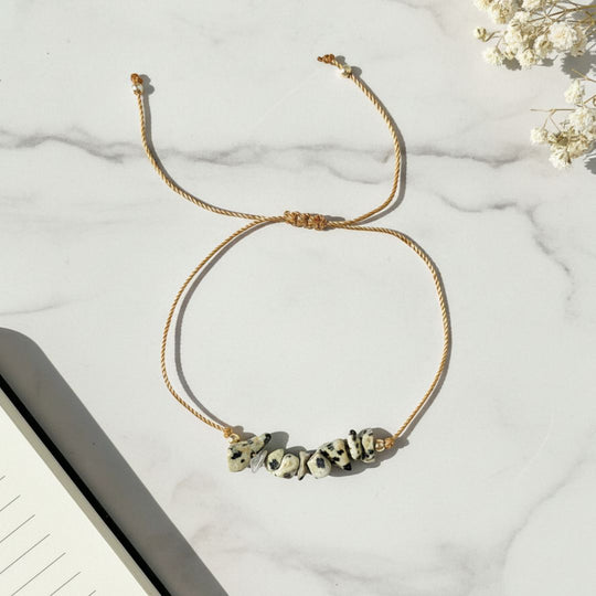 Golden thread bracelet with dalmatian jasper stone beads on a marble surface