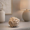 Decorative beige ball on a shelf with a lamp and vase in the background