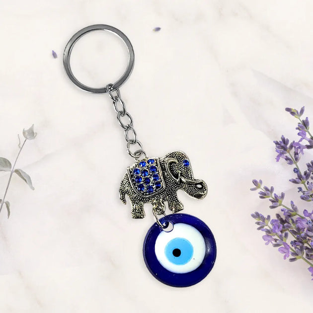 Keychain with elephant and evil eye charm on a white background with lavender flowers.