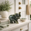 Decorative green elephant figurine on a white surface with a plant and books in the background.