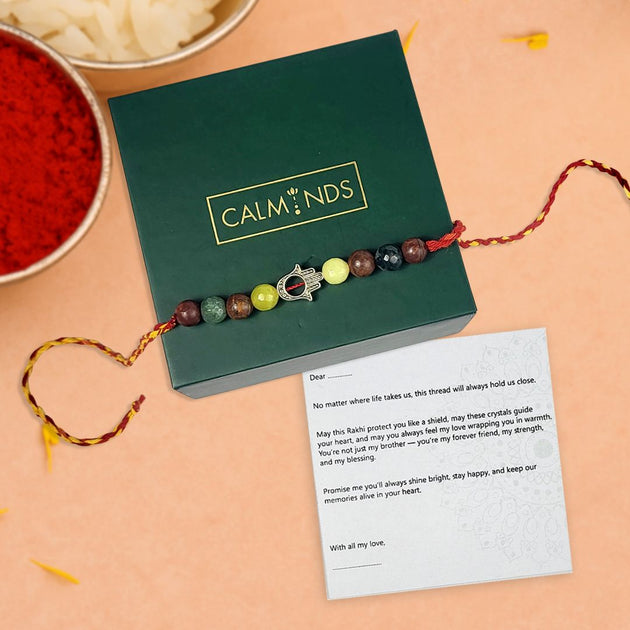 Colorful beaded rakhi with a message card on a green box, set against a beige background.