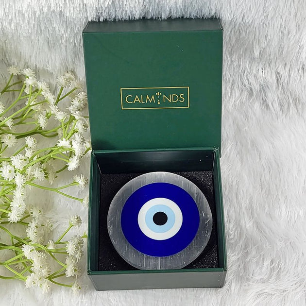 Decorative circular selenite plate with blue and white center in a green calminds box on a white background with flowers.