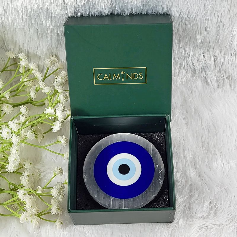 Decorative circular selenite plate with blue and white center in a green calminds box on a white background with flowers.