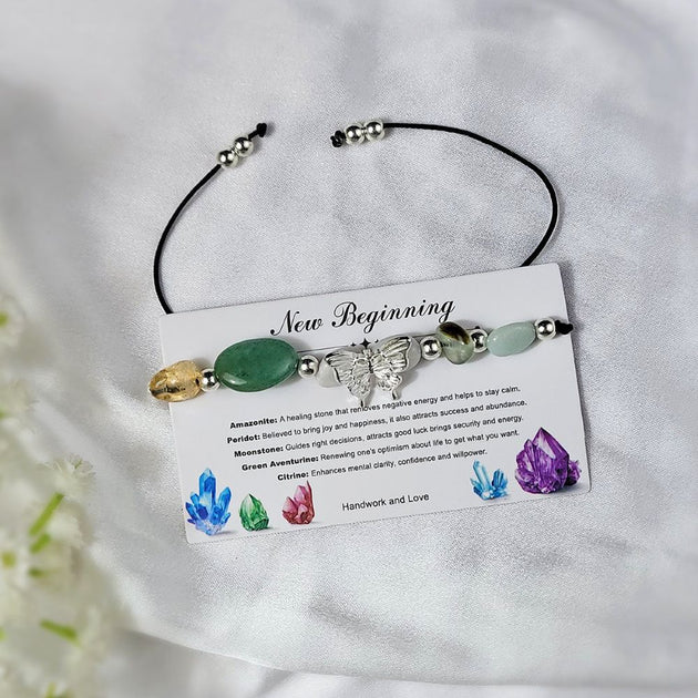 Bracelet with stones and a butterfly charm on a card labeled 'New Beginning' against a white background.