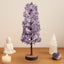 Decorative purple tree with a candle, statue, and crystal on a wooden surface.