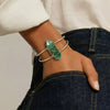 Gold bracelet with a green gemstone on a wrist against a neutral background