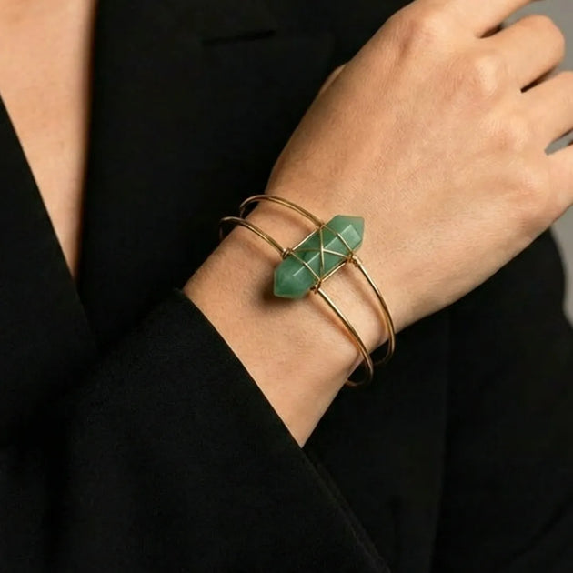 Gold bracelet with a green gemstone on a person's wrist against a black background