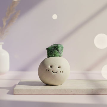 Ceramic smiley face vase with a green crystal on top, placed on a light surface with a soft, blurred background.