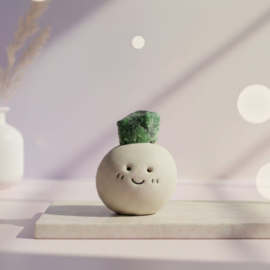 Ceramic smiley face vase with a green crystal on top, placed on a light surface with a soft, blurred background.