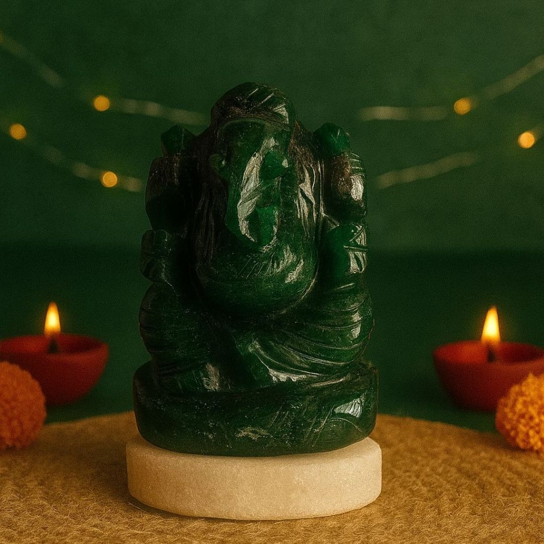 Green  stone statue of ganesha on a beige pedestal with red candles and orange flowers against a green background.