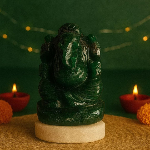 Green  stone statue of ganesha on a beige pedestal with red candles and orange flowers against a green background.