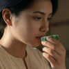 Woman drinking from a green cup with a warm, soft background