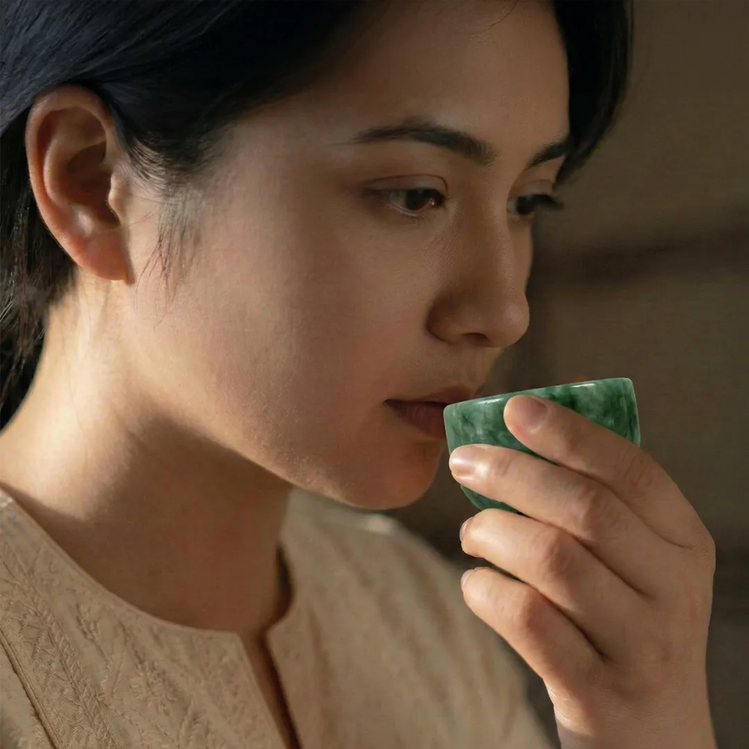 Woman drinking from a green cup with a warm, soft background